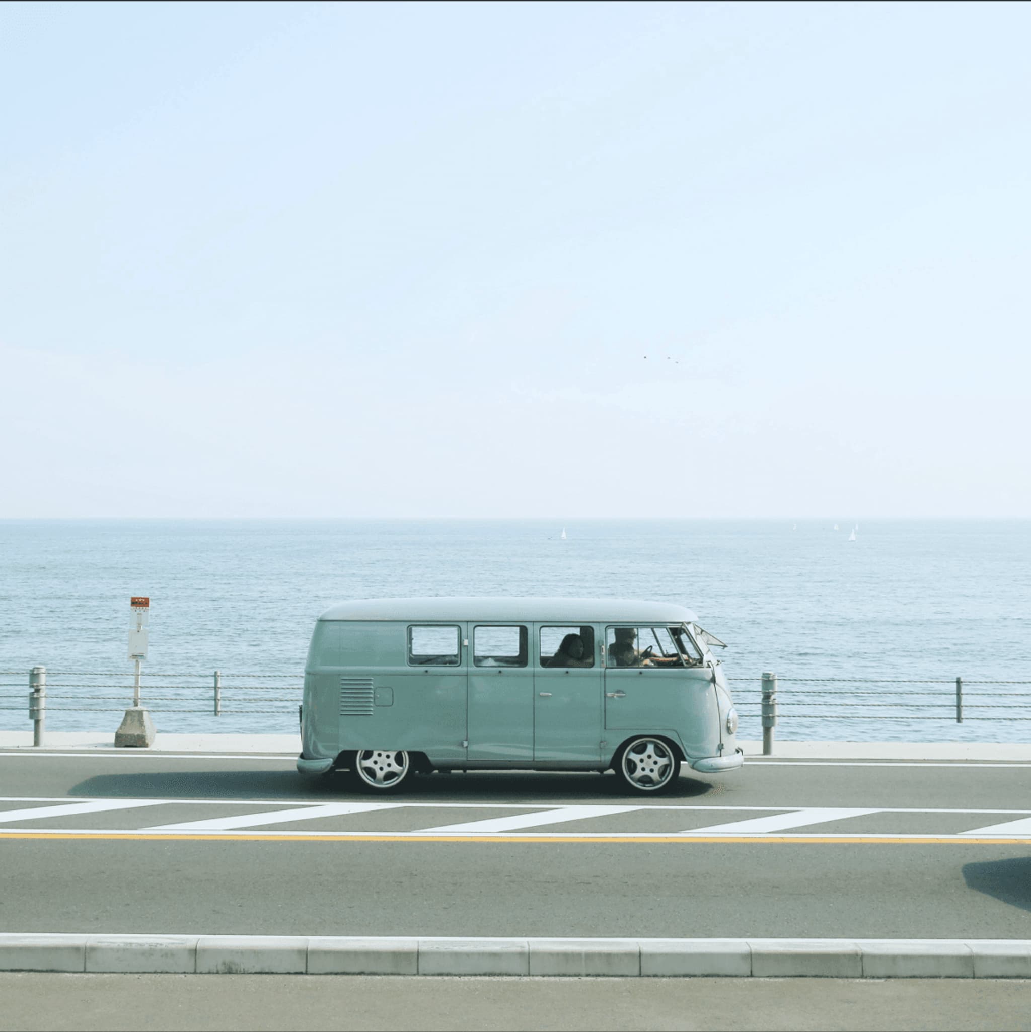 Vintage van parked near a seaside road with a clear blue sky and ocean in the background.