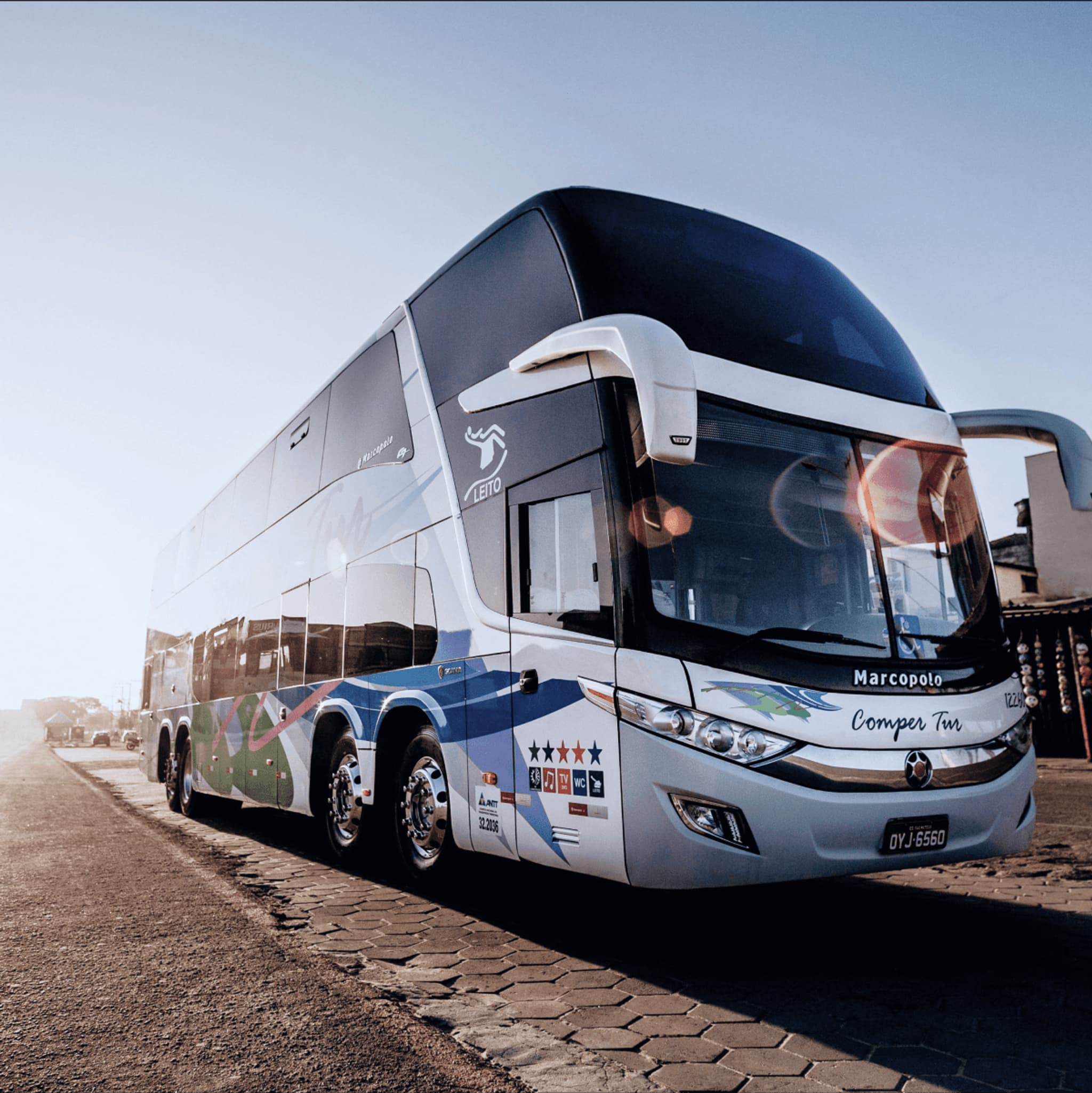 Luxury double-decker bus parked by the waterfront during sunset, featuring modern design and company branding.