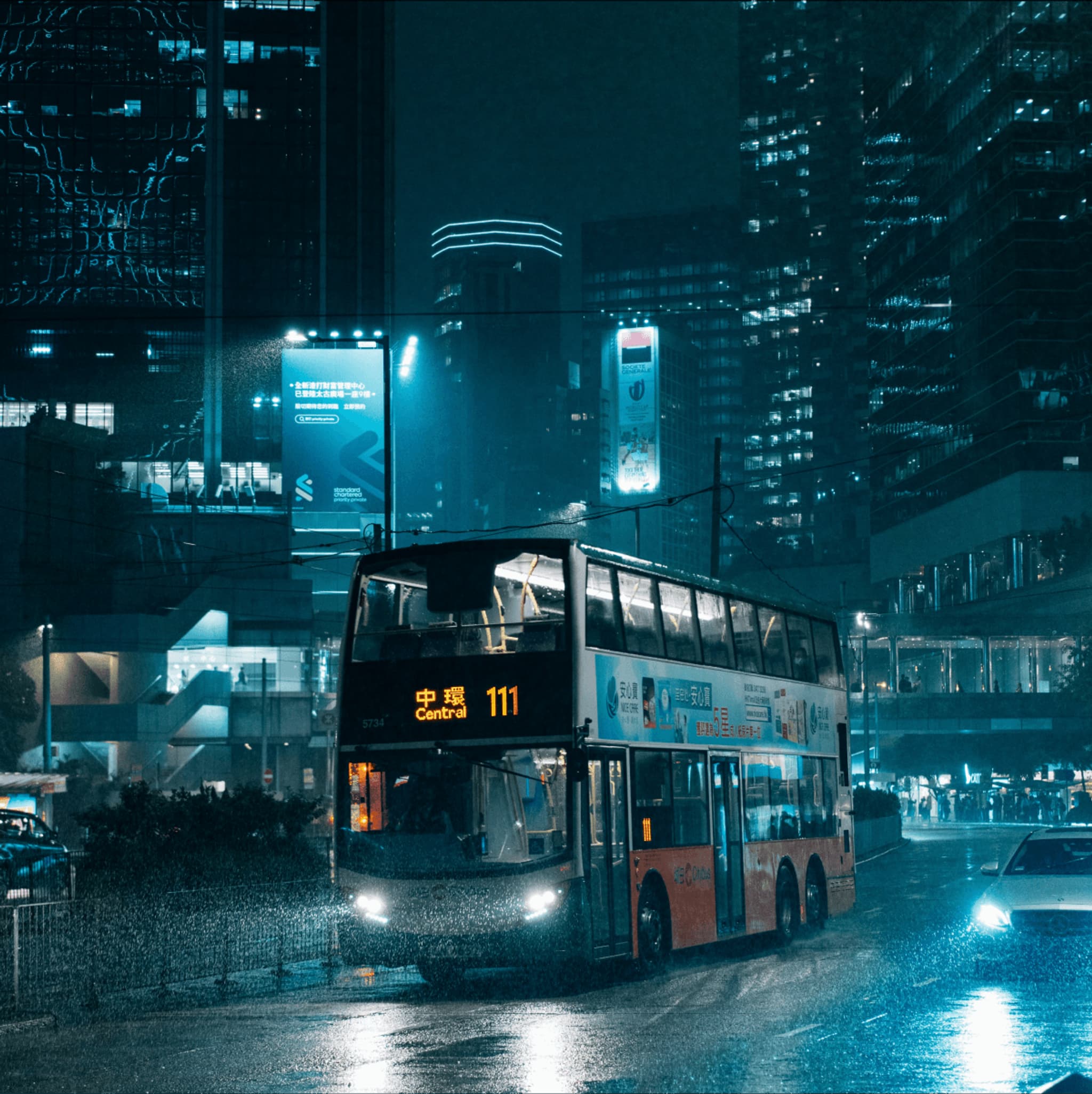 Double-decker bus at night in a cityscape, illuminated by neon lights and surrounded by modern buildings.