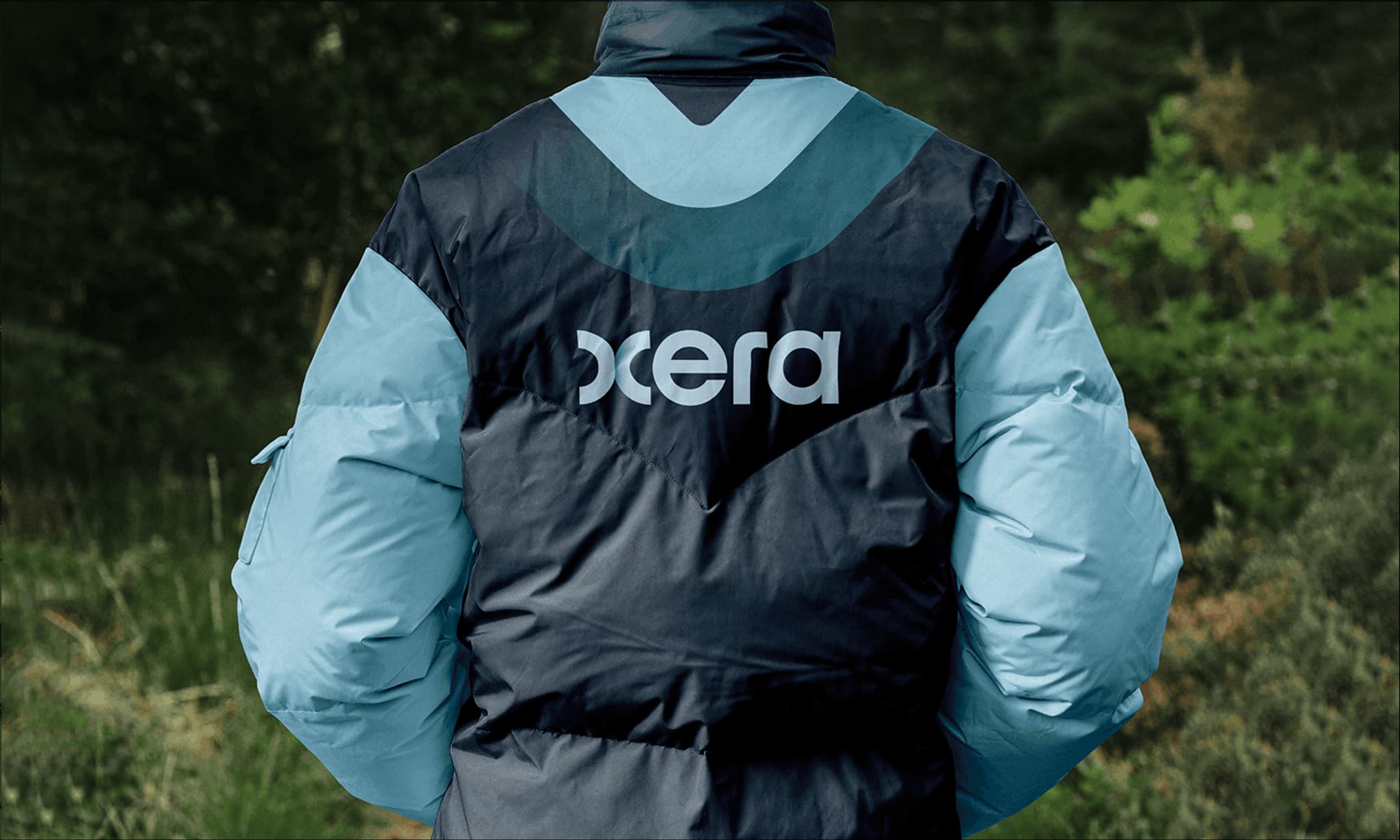 Blue and black puffer jacket featuring the "Oxera" logo, set against a natural outdoor background.